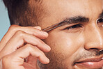 Closeup of one handsome young indian man using a tweezer to remove hair from his eyebrows. Face of a mixed race guy using beauty tool in his skincare treatment routine. Hand of a man holding a tweezer grooming himself