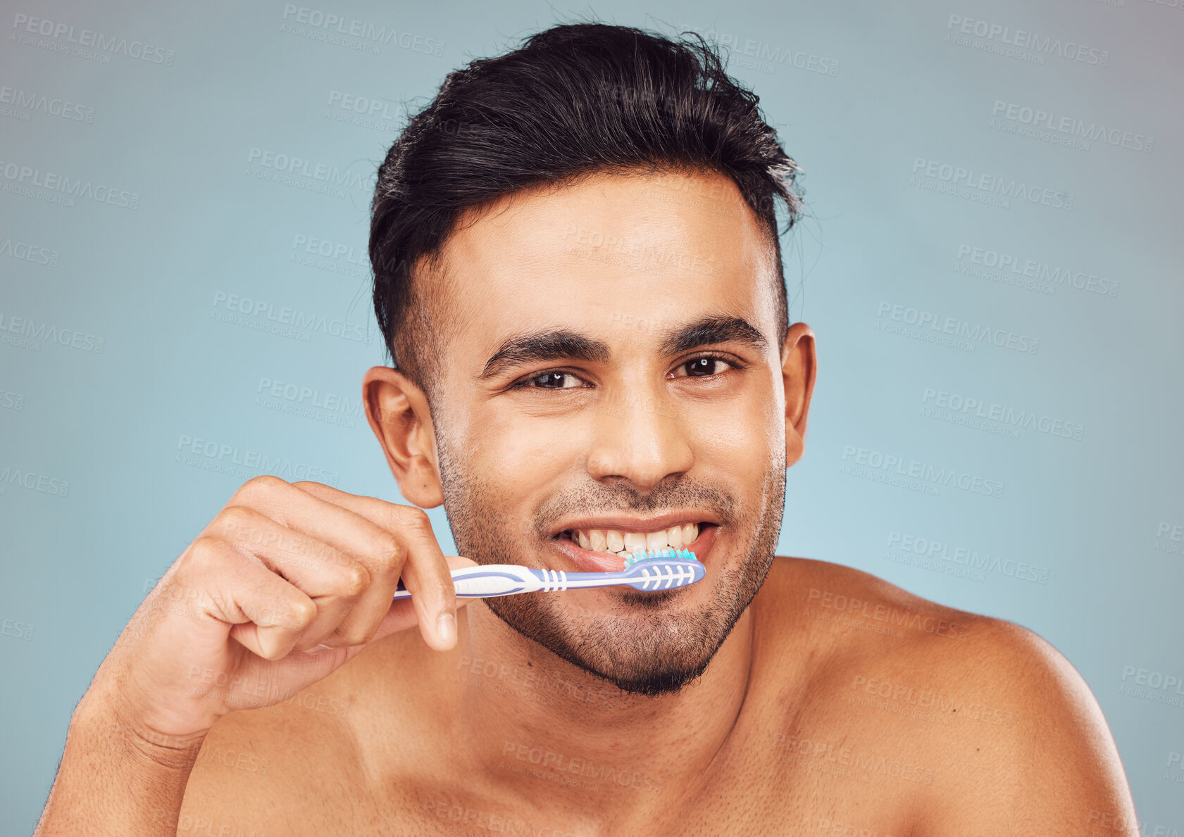 Buy stock photo Portrait of one smiling young indian man brushing his teeth against a blue studio background. Handsome guy grooming and cleaning his mouth for better oral and dental hygiene. Brush twice daily to prevent tooth decay and gum disease