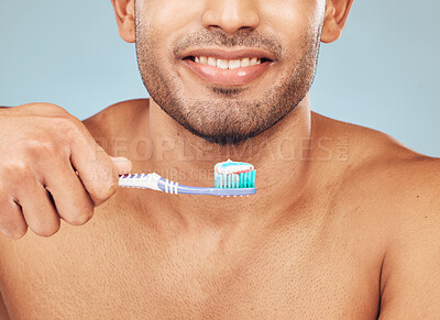 Buy stock photo Closeup of one mixed race man brushing his teeth against a blue studio background. Guy grooming and cleaning his mouth for better oral and dental hygiene. Brush twice daily to prevent tooth decay and gum disease