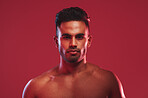 Closeup portrait of bare chested athletic young man posing against a red background. Handsome young masculine hispanic man posing in the studio