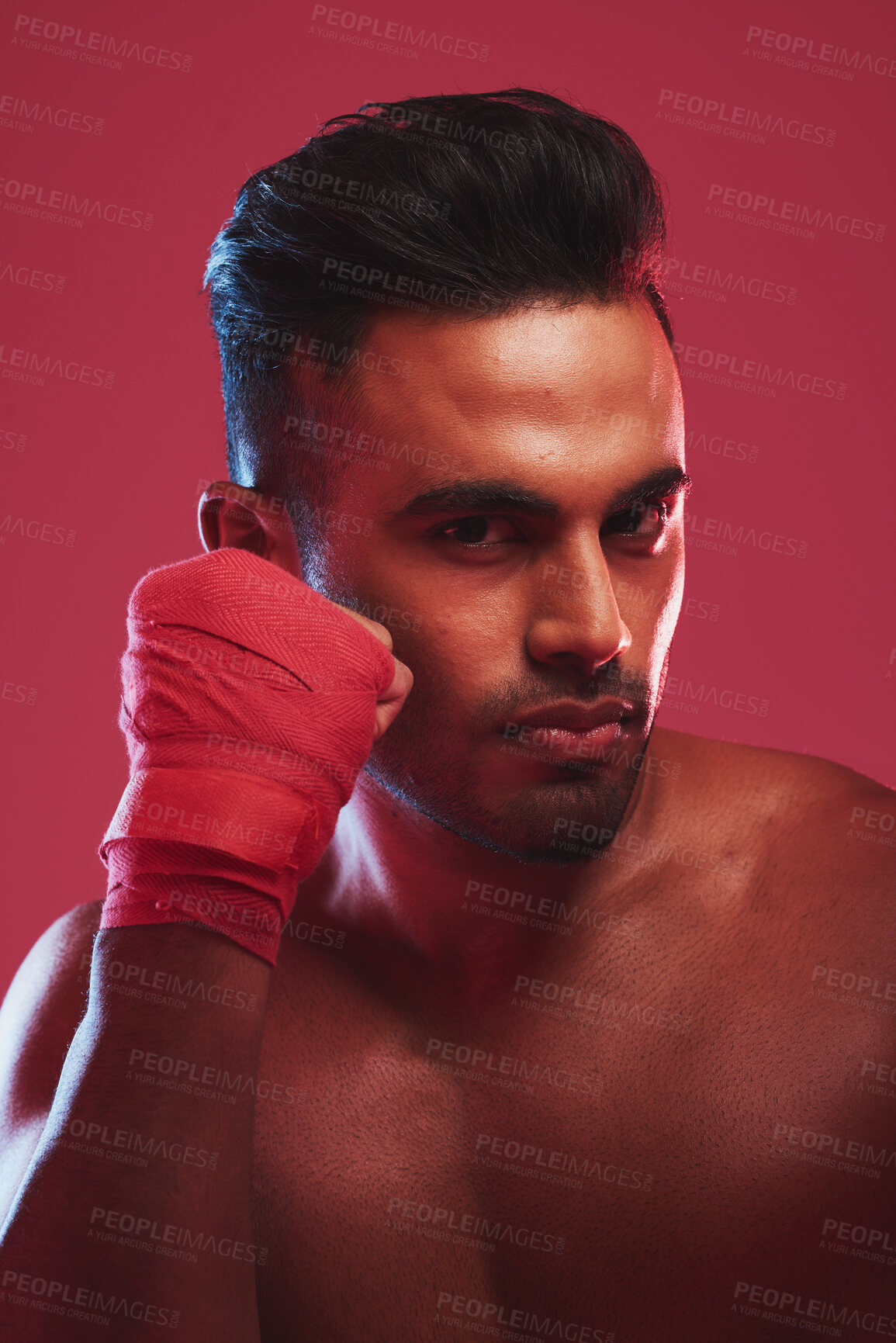 Buy stock photo Portrait of one fit and strong handsome mixed race kickboxer isolated against a red studio background and getting ready to fight. Hispanic man posing shirtless in a punching stance. Focused on target
