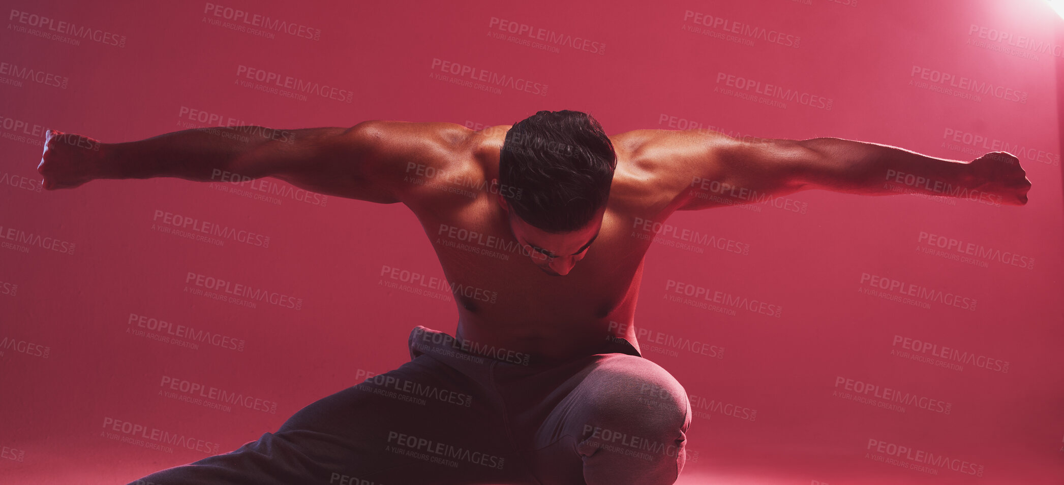 Buy stock photo One strong indian man stretching arms while crouching against a red studio background. Fierce muscular and topless man with toned body looking ready to fight or demonstrate powerful martial arts moves