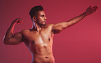 Masculine man standing shirtless with his fist closed and showing fighting technique while posing against a red studio background. Fit indian fighter ready to throw a punch  