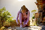 Full body fit and active african american woman crouching down to tie her shoelaces while hiking in nature. Athletic black woman tightening laces to prevent from tripping and getting ready to explore