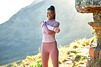 Smiling young african american woman hiking on a trail, stretching her arms and shoulder. Portrait of a smiling young athletic woman doing a warmup before hiking in nature on a mountain in the morning