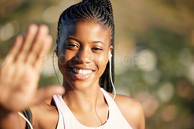 Young african american woman, hand raised in stop gesture while working out in nature. Portrait of fit woman smiling, listening to music in earphones exercising outside. Relaxed happy athletic woman