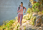 Young fit and active african american woman hiking and jogging through the mountains on a sunny summer day. Black woman running alone exercising and carrying a backpack while exploring nature looking determined and focused while wearing her sportswear out