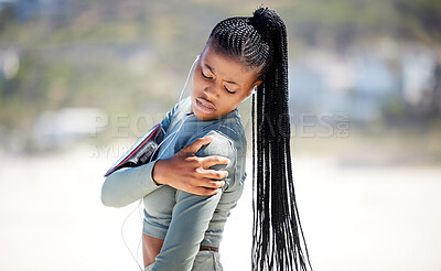 Fit and active young african american woman listening to music through earphones and suffering from shoulder pain during outdoor workout on a beach. Black athlete holding injured arm after exercising