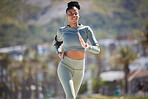 Fit and active African American woman listening to music through earphones and running alone in the city. Black woman focused on fitness and speed while jogging and wearing her phone in an arm holder 