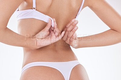 Rear view of one unrecognizable model posing in underwear against a white background studio. Unknown hispanic female removing her bra while showing her thick shape in a studio
