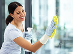A happy smiling mixed race domestic worker using a cloth on a window. One Hispanic woman enjoying doing chores in her apartment