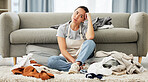 A young mixed race domestic cleaner looking distracted and overwhelmed while folding laundry. A beautiful Asian woman daydreaming while doing household chores in her apartment