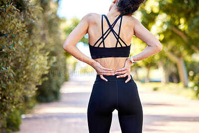One mixed race woman from behind holding sore lower back while exercising outdoors. Female athlete suffering with painful spine injury from fractured joint and inflamed muscles during workout. Struggling with stiff body cramps causing discomfort