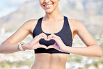 Closeup of one confident young mixed race woman gesturing a heart shape with her hands while exercising outdoors. Happy female athlete caring for body with regular training workout or run. Endorsing a healthy active lifestyle