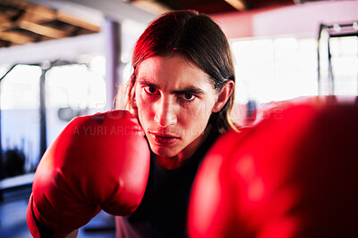 Portrait of one fit young caucasian man wearing boxing gloves with neon red light reflecting on face while training in a gym. Strong focused boxer practising for competition fight. Fierce guy ready to strike with a hit and jab while learning self defence
