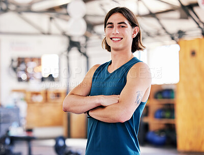 Portrait of one confident young strong caucasian man standing with his arms crossed ready for training in a gym. Happy guy smiling while working as a trainer and instructor in a fitness centre