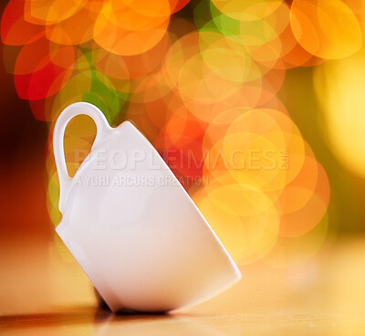 Closeup of a cup isolated against a colourful bokeh background. White teacup tilted on the side on a table. Crockery to enjoy a warm beverage from such as tea or coffee in a cafe or at home