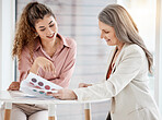 Two happy caucasian businesswomen having a meeting at a table in an office at work. Female businesspeople going through paper and colour swatches together at work