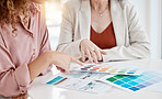 Closeup of two businesspeople looking at colour swatches while in a meeting together at work. Businesswomen choosing between different colours for a design in an office at work