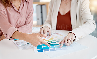Closeup of two businesspeople looking at colour swatches while in a meeting together at work. Businesswomen pointing their fingers and choosing between different colours for a design in an office at work