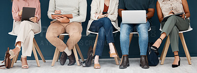 Group of businesspeople sitting on chairs in a row in an office together. Five business professionals sitting using technology in a waiting room together in an office