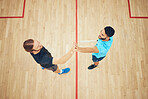 Above view of two athletic squash players giving high five before game on court. Team of fit active caucasian and mixed race male athletes using before competing and training together in sports centre