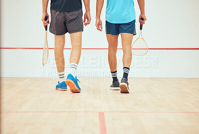 Rear view of two unknown squash players walking together on court and holding rackets before game. Fit active mixed race and caucasian athlete getting ready for training and practice in sports centre