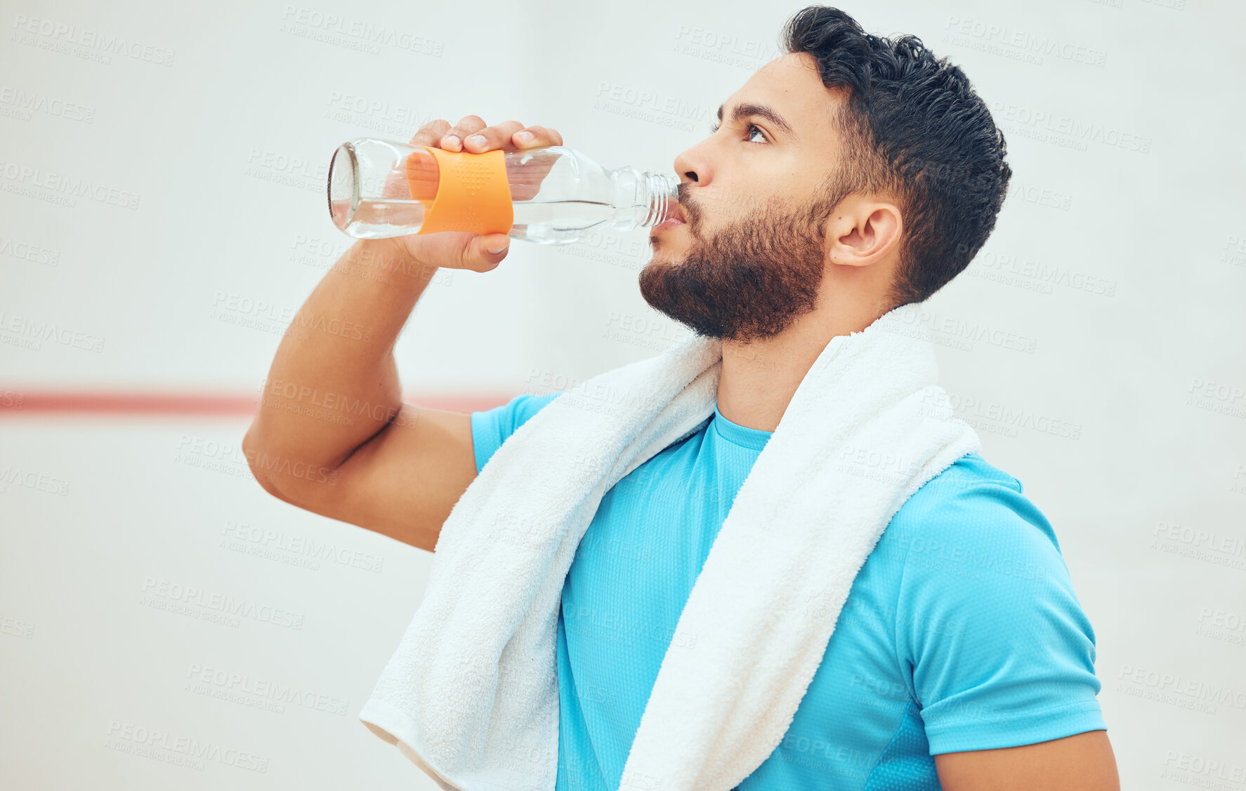 Buy stock photo Young athletic squash player standing alone and drinking water after playing court game. Fit active mixed race athlete resting after training practice in sports centre. Hispanic sporty man on break