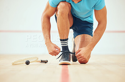 Unknown athletic squash player kneeling and tying shoelaces before playing court game with copyspace. Fit active mixed race athlete getting ready for training practice at sport centre. Sporty hispanic
