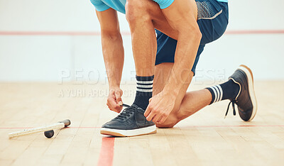 Unknown athletic squash player kneeling and tying shoelaces before playing court game. Fit active mixed race athlete crouching and getting ready for training practice at sport centre. Sporty hispanic