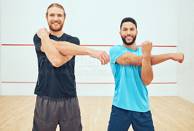 Portrait of two squash players stretching and smiling before playing court game. Happy fit caucasian and mixed race athlete standing together and getting ready for training practice in sports centre