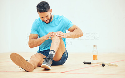 Young athletic squash player suffering from knee injury while playing a game on court with copyspace. Full length fit active mixed race athlete sitting alone and feeling pain and touching leg joint