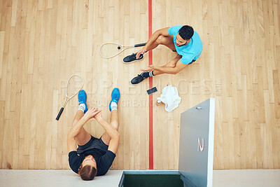 Above view of two unknown athletic squash players sitting together after playing court game. Fit active mixed race and caucasian athletes resting after training practice in sports centre. Sporty men