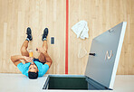 Above view of young athletic squash player sitting alone and drinking water after playing on court. Fit active mixed race athlete resting after training practice in sports centre. Hispanic sporty man