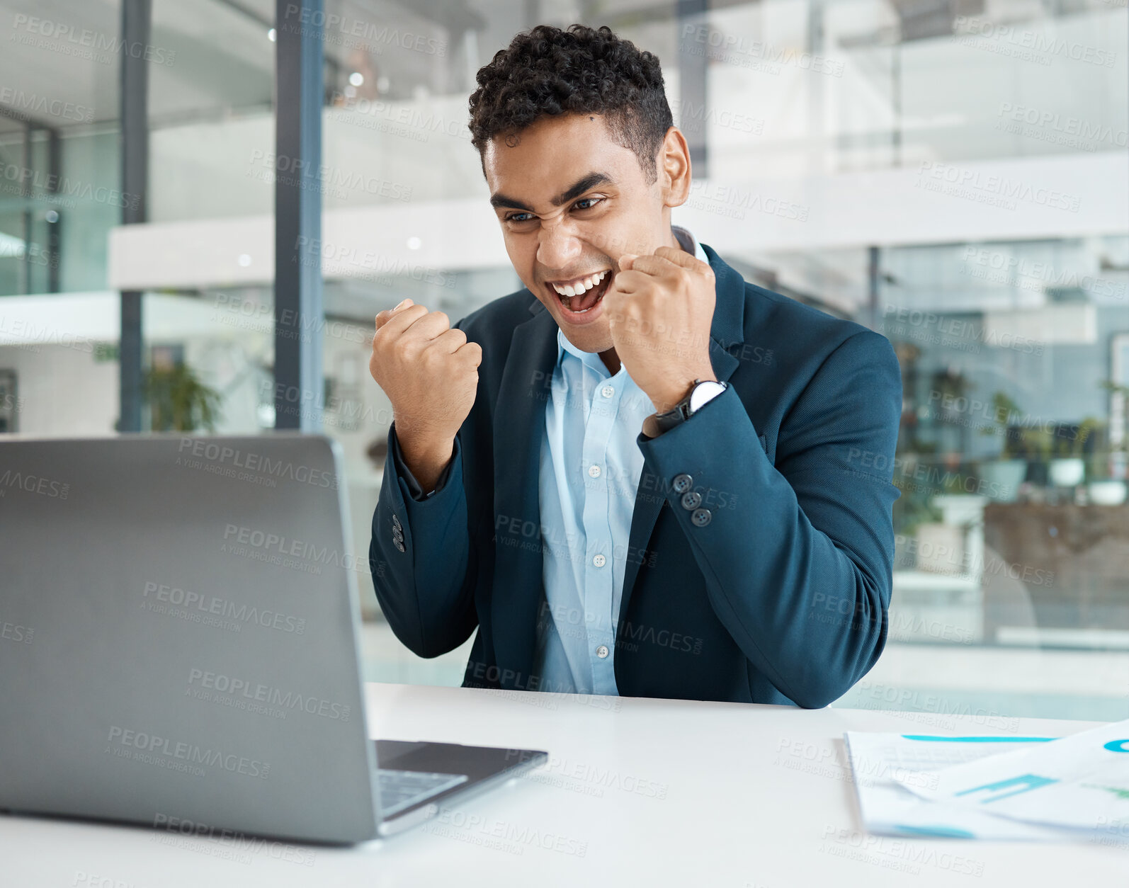 Buy stock photo Young mixed race businessman cheering with passion while working on a laptop alone at work. One hispanic businessperson smiling and celebrating victory working at a desk in an office