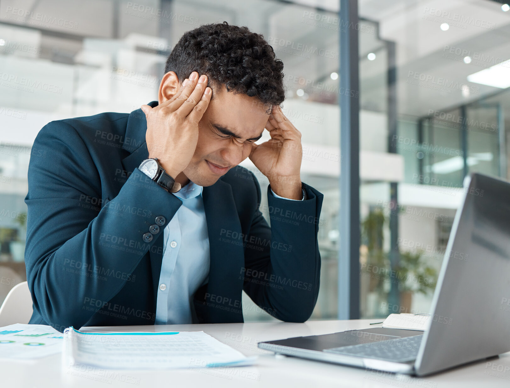 Buy stock photo Young angry mixed race businessman suffering from a headache while upset and working on a laptop at work. One hispanic businessperson looking stressed working at a desk in an office
