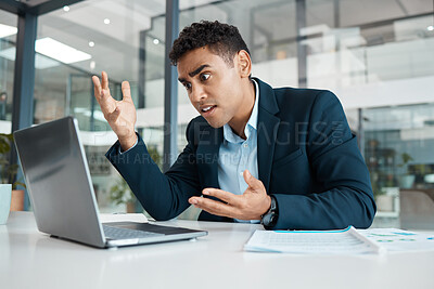 Young angry mixed race businessman working on a laptop at work. One hispanic businessperson looking stressed and upset working at a desk in an office