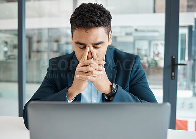 Young mixed race businessman suffering from a headache while working on a laptop alone at work. One hispanic businessperson looking stressed and upset working at a desk in an office