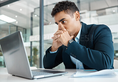 Buy stock photo Young mixed race businessman looking stressed while working on a laptop alone at work. Hispanic businessperson looking worried working at a desk in an office