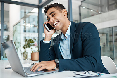 Young happy mixed race businessman talking and laughing on a call using a phone and typing on a laptop alone at work. One cheerful hispanic male businessperson smiling while talking on a cellphone and using a laptop in an office