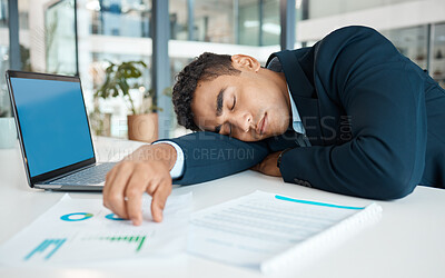 Young mixed race businessman resting and working on a laptop at a table alone at work. One stressed hispanic businessperson sleeping while working at a desk in an office
