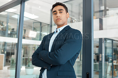 Young serious mixed race businessman standing with his arms crossed alone at work. One confident hispanic male boss standing in an office