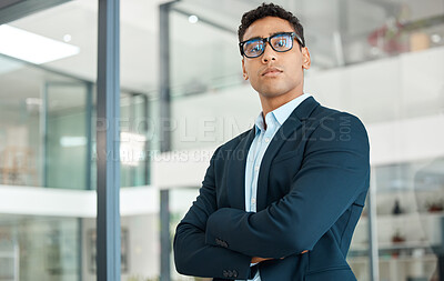 Young serious mixed race businessman standing with his arms crossed alone at work. One confident hispanic male manager wearing glasses standing in an office