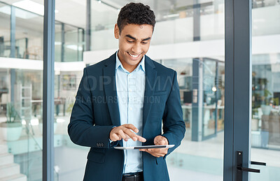 Buy stock photo Young happy mixed race businessman holding and working on a digital tablet alone at work. One content hispanic male businessperson smiling and using social media on a digital tablet in an office