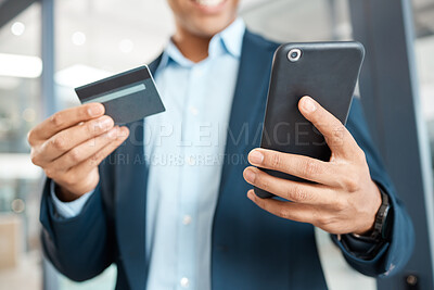 Buy stock photo Closeup of a mixed race businessman holding and using a credit card and phone alone at work. One hispanic male businessperson making an online purchase with his debit card and cellphone