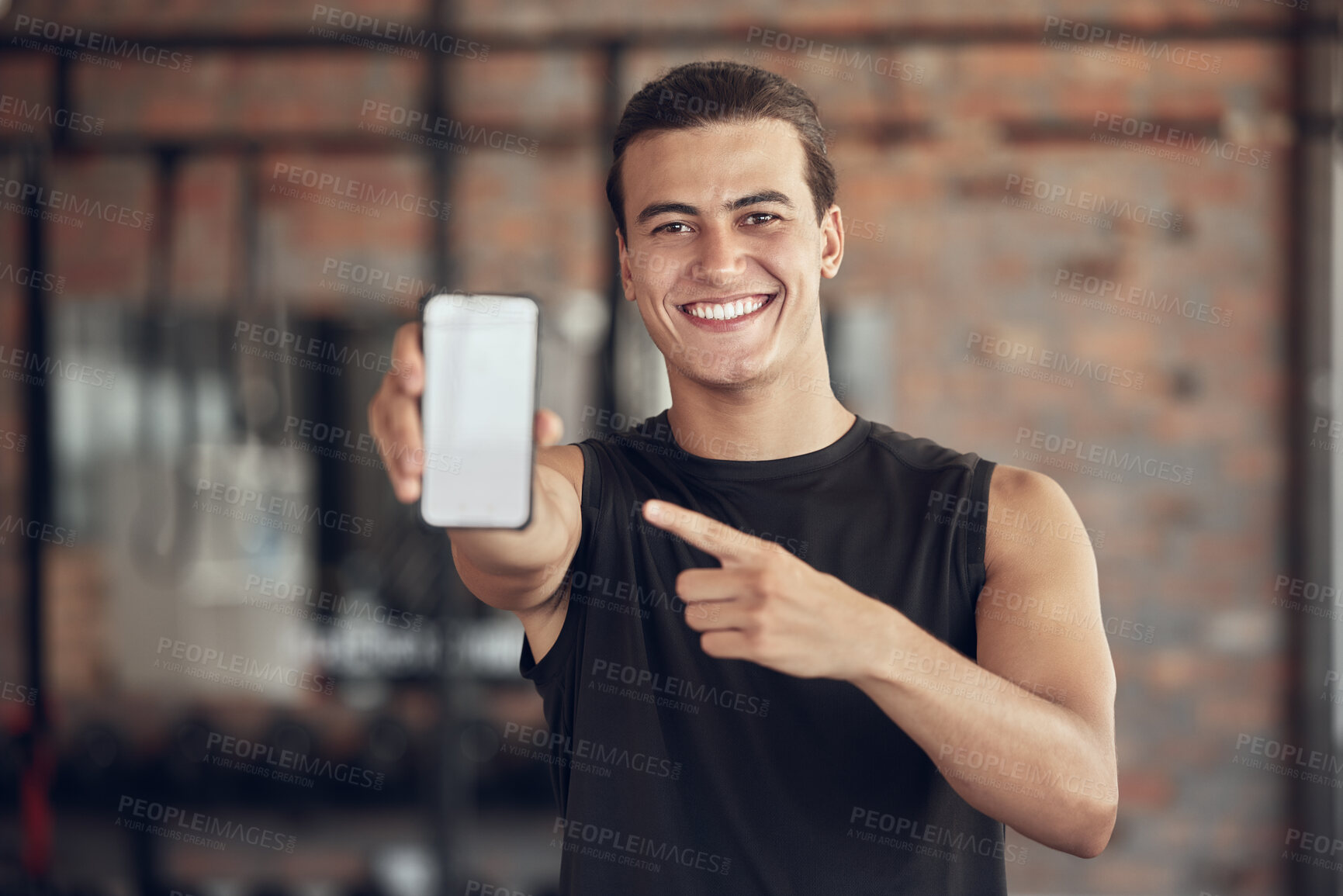 Buy stock photo Happy man pointing to his phone in the gym. Portrait of a young man taking a break from exercise to use his cellphone. man online on his cellphone at the gym. Man gesturing toward his mobile phone