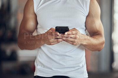 Man using his cellphone in the gym. Man browsing an app online on his smartphone. Bodybuilder taking a break from working out to text on his cellphone. Athlete using his cellphone in the gym
