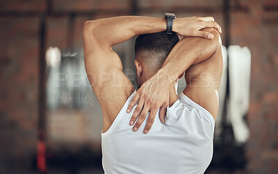 Back of a bodybuilder stretching before exercise. Athlete doing an arm warmup before a workout. Behind fit muscular man doing a shoulder stretch before exercise. Athlete preparing to workout.