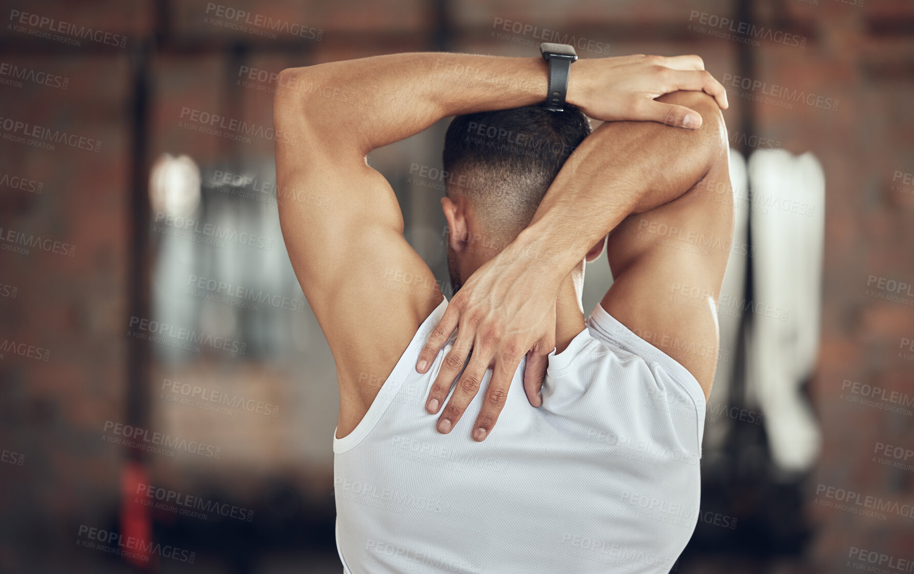 Buy stock photo Back of a bodybuilder stretching before exercise. Athlete doing an arm warmup before a workout. Behind fit muscular man doing a shoulder stretch before exercise. Athlete preparing to workout.