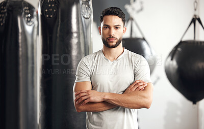 Portrait of one serious young hispanic man standing with his arms crossed ready for exercise in a gym. Muscular mixed race instructor looking focused and motivated for training workout in a fitness centre